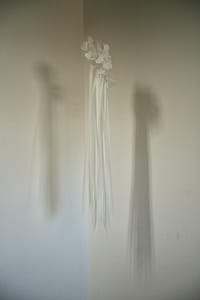 A suspended Dura-lar sculpture with petal like pieces and long thin pieces tied together with thin metal wire.