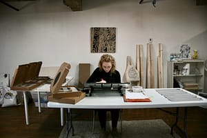 An image of myself carving a lino block at a desk surrounded by art supplies