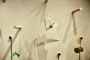 A sculpture with one long strip hung from the centre tied with mixed-media materials that are hung from a dowel.