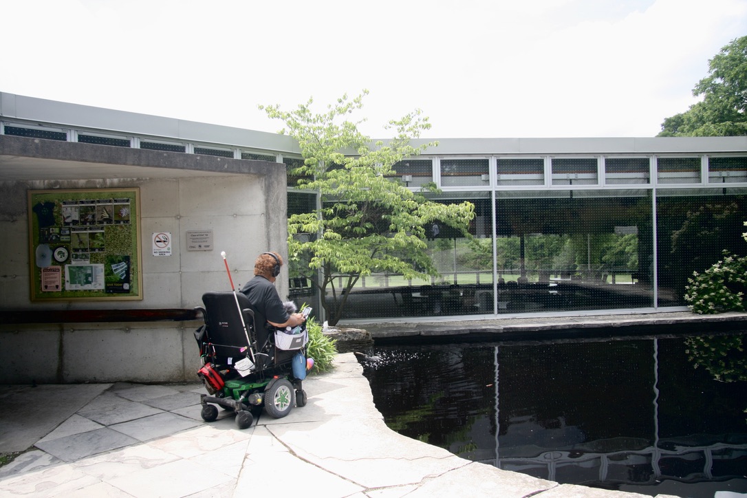 A participant in a wheelchair looks over a pond next to the Arboretum Centre building.