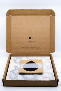 Image description: An open cardboard box with Olivia Brouwer's logo, website, and Instagram printed on the back in English text and Braille. The CONTACT artwork and booklet are displayed inside the box.