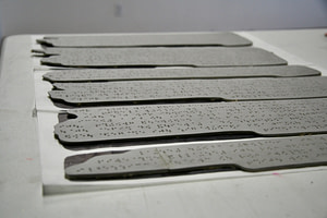 A collection of lino plates cut into paragraphs with Braille holes cut into each segment.