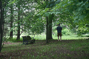 A participant is captured taking a recording from the forest next to a rotting bench.