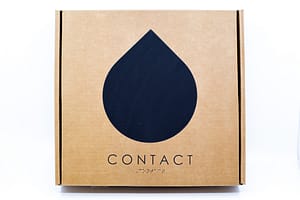 Image description: A square cardboard box with a black teardrop shape in the centre. The title, "CONTACT", is in English text and Braille beneath the image.